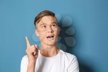 Emotional teenage boy with raised index finger on color background�
