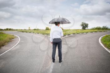 Businessman with umbrella standing at crossroads. Concept of choice�