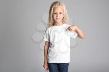 Cute little girl pointing at her t-shirt on grey background�