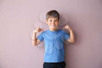 Cute little boy pointing at his t-shirt on color background�