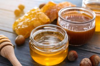 Full jars of honey with honeycomb on wooden table, closeup�