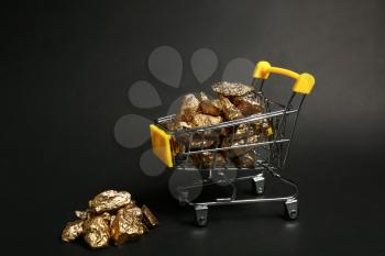 Small shopping cart with gold nuggets on dark background�