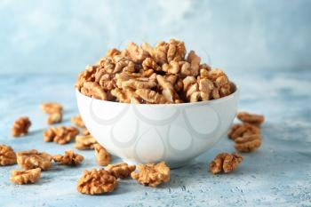 Bowl with tasty walnuts on color table�