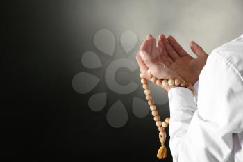 Young Muslim man with rosary beads praying on dark background, closeup�