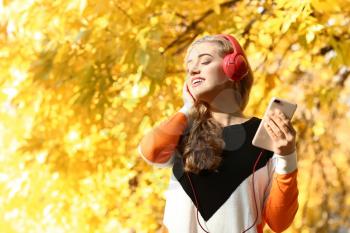 Beautiful young woman listening to music in autumn park�