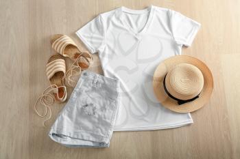 Composition with white t-shirt, shorts, hat and shoes on wooden background�