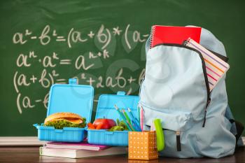 Backpack with school supplies and lunch box near chalkboard�