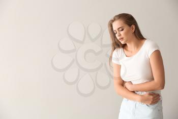 Young woman suffering from abdominal pain on light background�