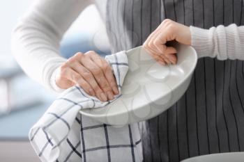 Woman wiping plate with towel in kitchen�