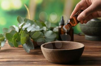 Woman pouring eucalyptus essential oil into bowl on wooden table�