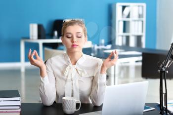 Beautiful businesswoman meditating at table in office�