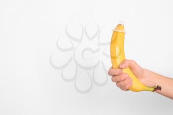 Woman holding banana with condom on light background. Erotic concept�