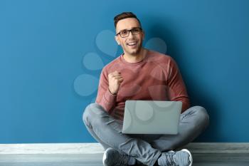 Successful young man with laptop sitting near color wall�
