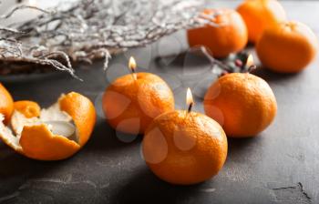 Tangerines with burning candle wicks on grunge table�