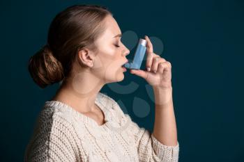 Young woman with inhaler having asthma attack on dark background�