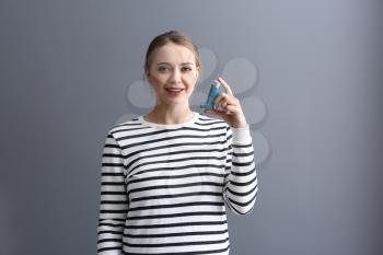 Young woman with inhaler on grey background�