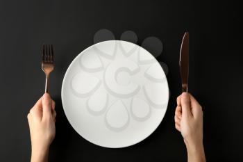 Female hands with cutlery and empty plate on dark background�