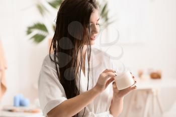 Young woman applying cream on beautiful long hair in bathroom�