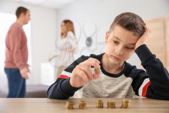 Sad little boy with coins and his quarreling parents at home. Concept of child support�