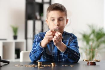 Sad little boy with coins sitting at table in lawyer's office. Concept of child support�