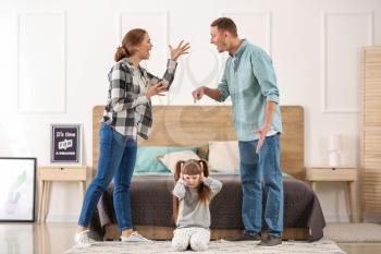 Sad little girl covering ears while her parents are arguing at home�