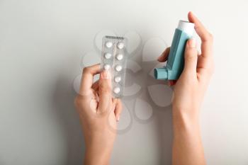 Female hands with inhaler and pills against asthma on light background�