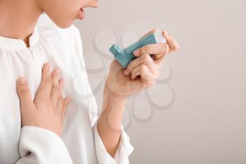 Young woman using inhaler against asthma on light background�