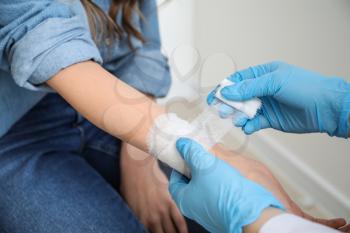 Doctor applying bandage onto wrist of young woman, closeup�
