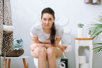 Young woman suffering from constipation on toilet bowl at home�