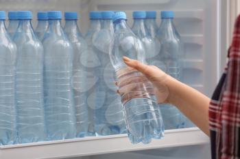 Woman taking bottle of water from fridge in shop�