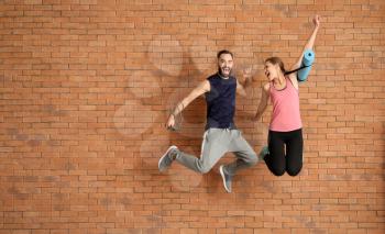 Young sporty people jumping against brick wall�