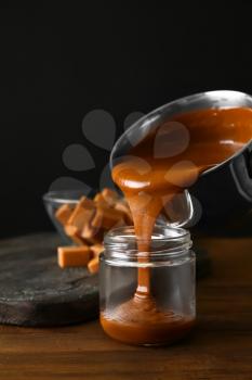 Liquid caramel pouring from pot into jar on table 