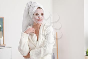 Beautiful young woman with sheet facial mask at home�