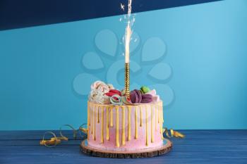 Tasty cake with firework candle on color table�