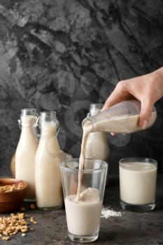 Woman pouring tasty vegan milk from bottle into glass on grey background�
