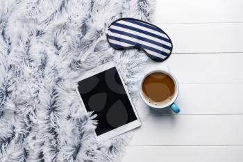 Composition with sleep mask, tablet computer and coffee on wooden background�