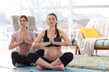 Doula with pregnant woman meditating at home�