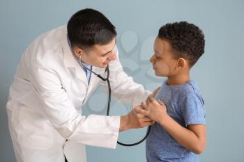 Pediatrician examining African-American boy on color background�