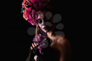 Young woman with painted skull on her face for Mexico's Day of the Dead against dark background�