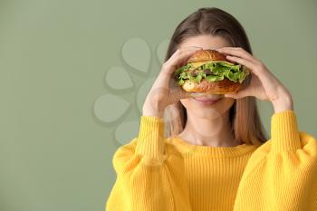 Beautiful happy young woman with tasty burger on color background�
