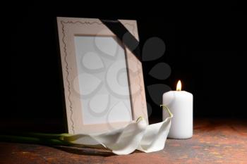 Blank funeral frame, burning candle and flowers on table against dark background�