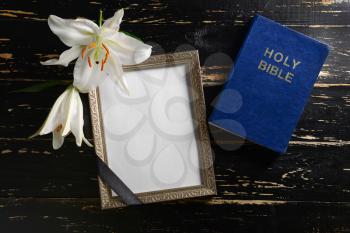 Blank funeral frame, flowers and Bible on dark wooden background�