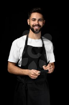 Handsome waiter with notebook on dark background�