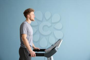 Sporty young man training on treadmill against color background�