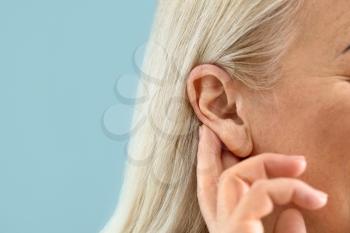 Mature woman with hearing problem on color background, closeup�