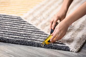 Woman with tape measure cutting carpet on floor�