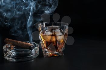 Glass of cold whiskey with cigar on dark background�