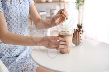 Woman drinking tasty frappe coffee at table�