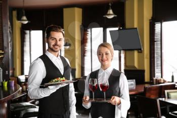 Young waiters with wine and salad in restaurant 