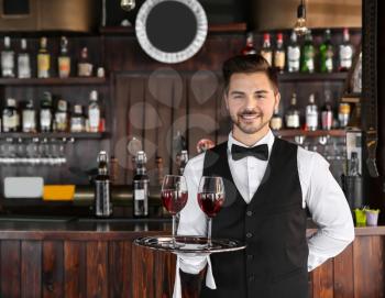Young male waiter with glasses of wine in restaurant�